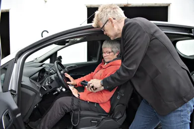 En kvinde sidder i en af HandicapBilistCentrets koerevogne, mens en ansat i HandicapBilistCentret tester indretningen.