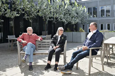 Tre personer sidder på bænke og stole udenfor