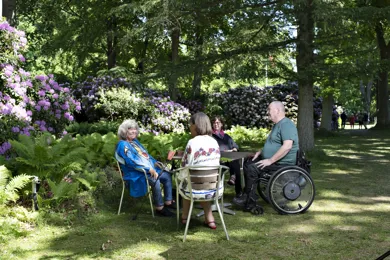 En gruppe mennesker sidder og snakker udendørs, den ene sidder i kørestol
