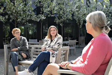 Tre kvinder sidder på en baenk og taler