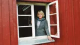 Jorunn står i åbent vindue i rødt hus