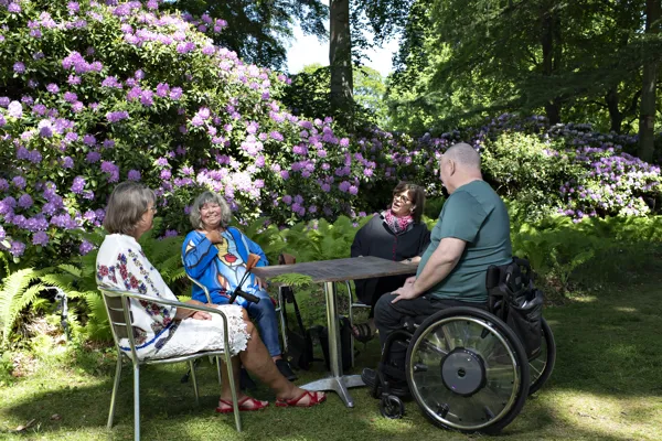 Fire personer sidder ved et bord og taler ude i naturen.