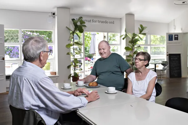Tre mennesker snakker sammen over kaffe og kage
